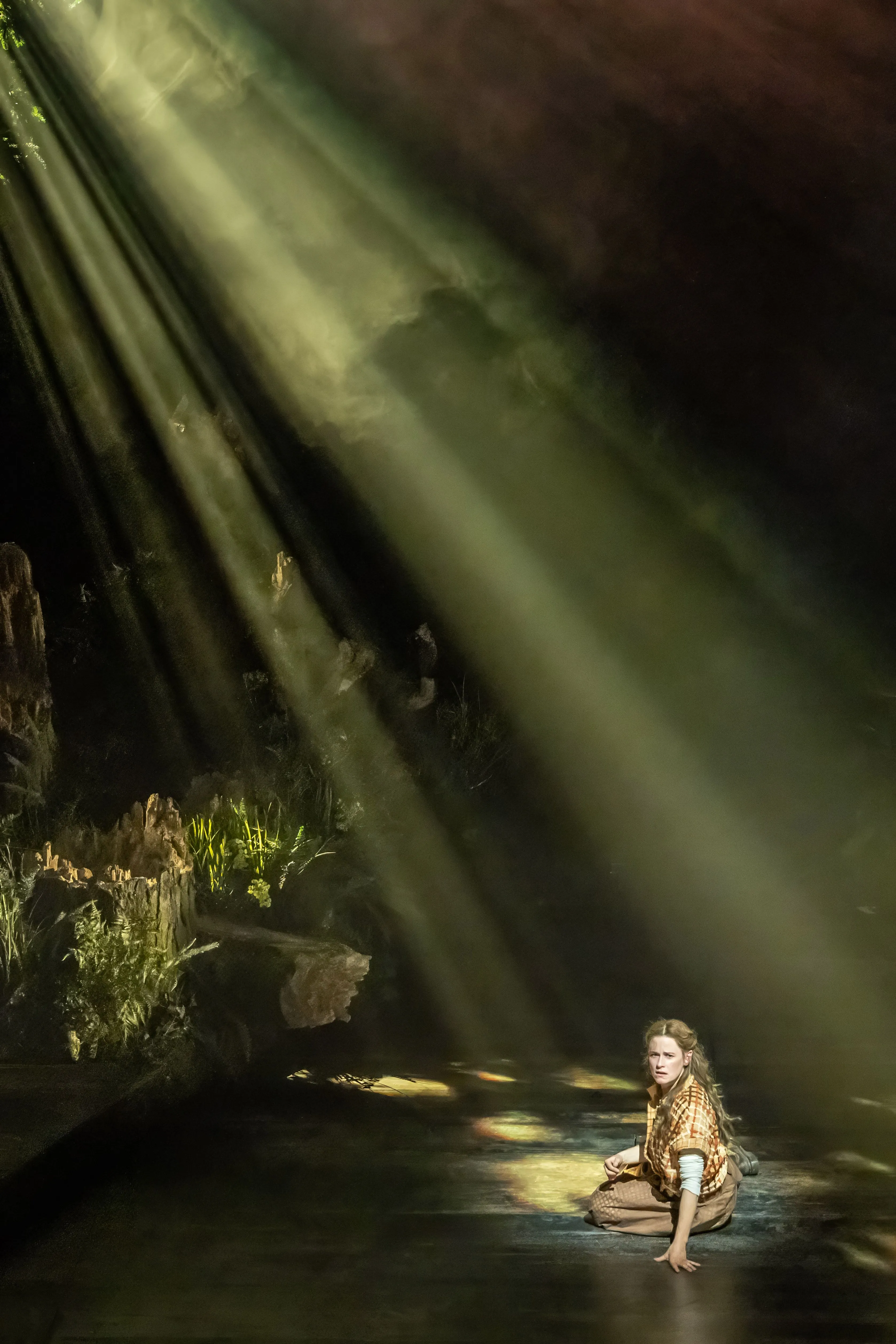 Shafts of light fall on a lone figure in the woods, original Bridge Theatre production photo